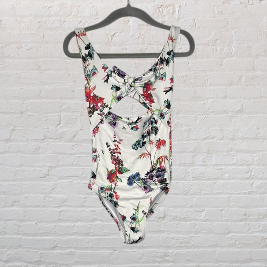 Women's floral cutout one-piece swimsuit with a bow detail, white base with multicolor flowers, hanging on a hanger.