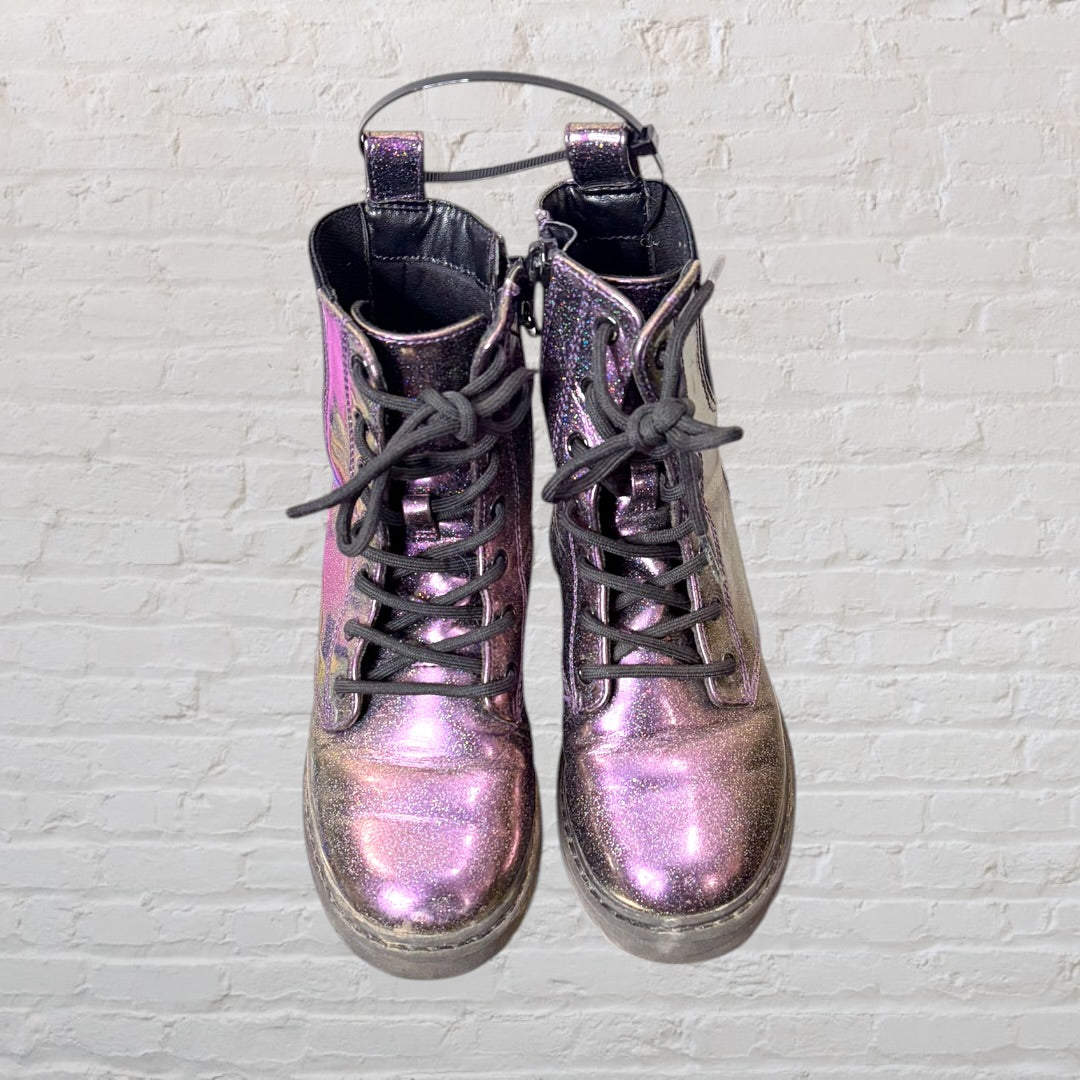 Pair of iridescent combat boots with black laces and thick soles against a white brick wall.
