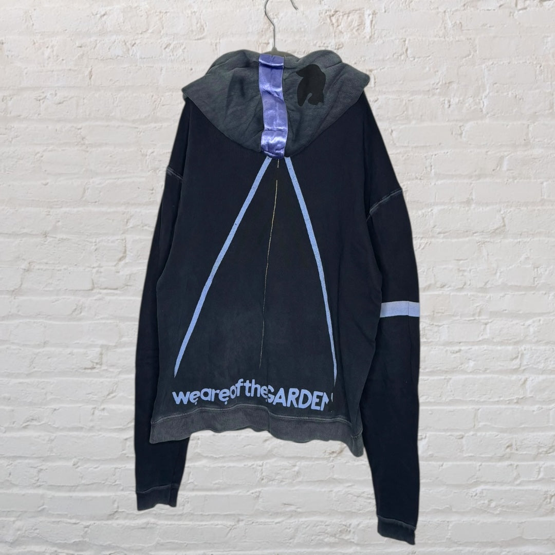 Black and grey hoodie with 'We Are of the Garden' text and graphic design on the back, displayed on a hanger.