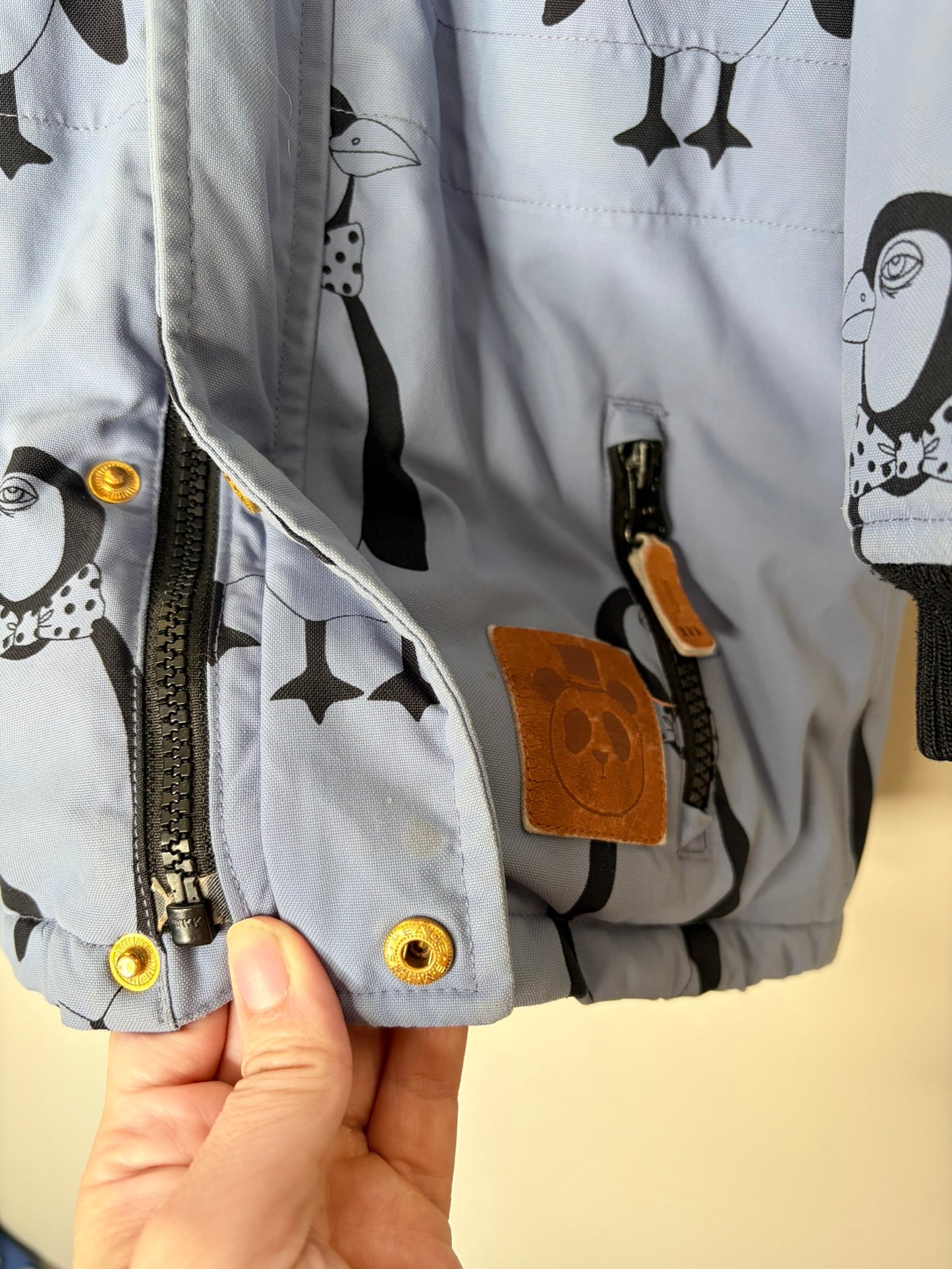 Grey parka with penguin print, featuring a faux fur trimmed hood and reflective patch on the sleeve.