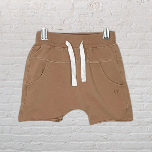 Tan casual shorts with white drawstring and pockets, displayed against a white brick background.