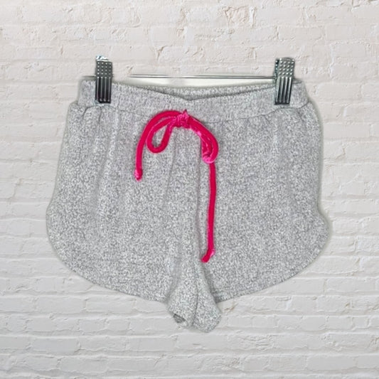 Gray sherpa knit shorts with a hot pink drawstring, displayed against a white brick background.
