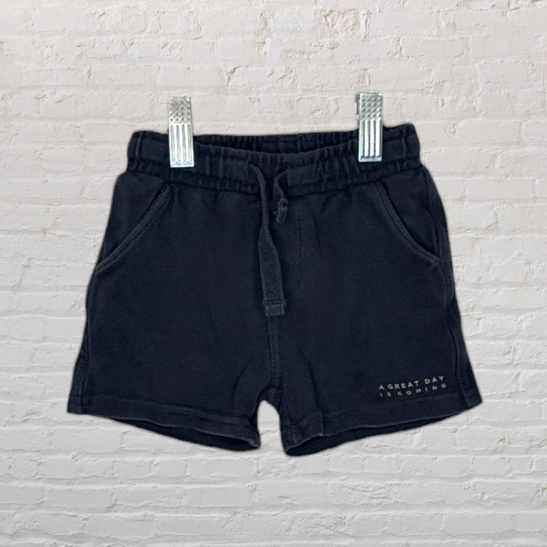Black casual shorts with a drawstring waist and text 'A great day is coming' on the side, hanging on clips.