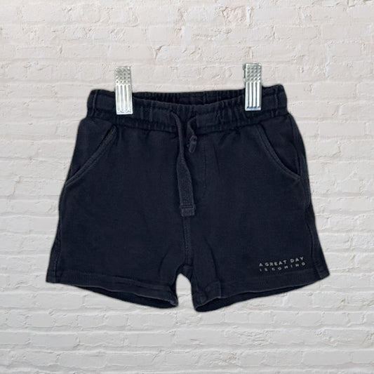 Black casual shorts with a drawstring waist and text 'A great day is coming' on the side, hanging on clips.