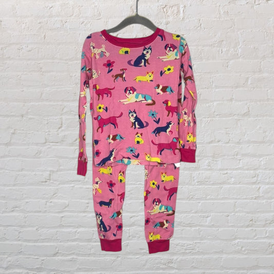 Pink kids' pajama set featuring various colorful dog prints, displayed on a hanger against a white brick wall.