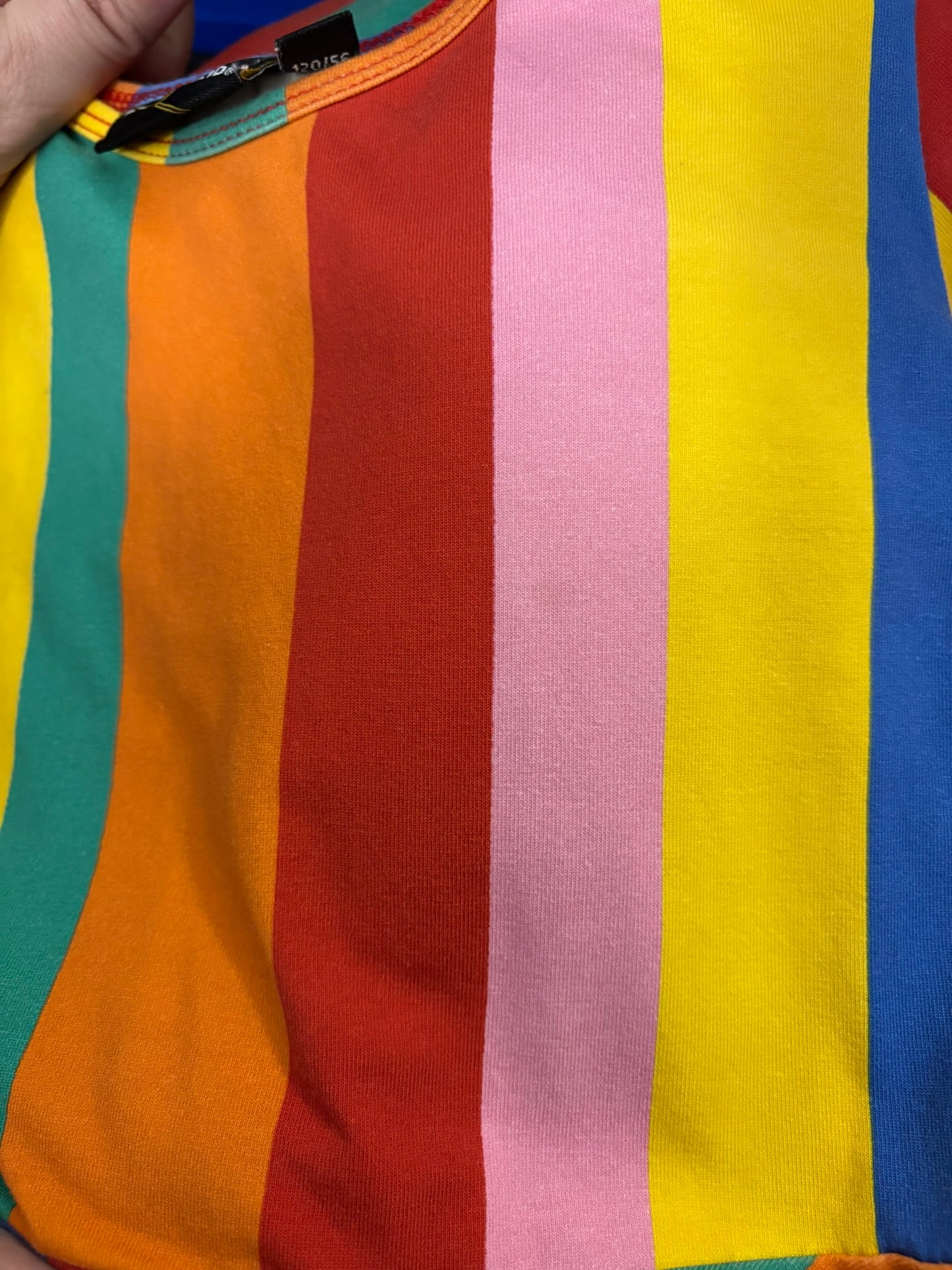 Vibrant rainbow-striped short sleeve dress with a fitted top and flared skirt, hanging on a hanger against a white brick wall.