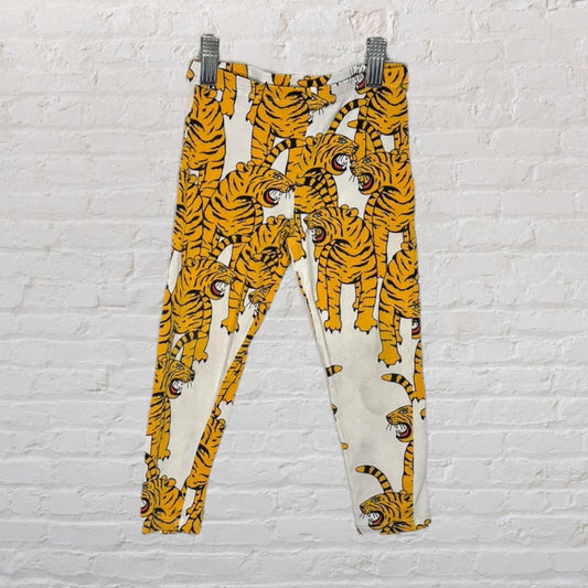 Vibrant leggings with all-over tiger print in yellow and black, hanging against a white brick wall.