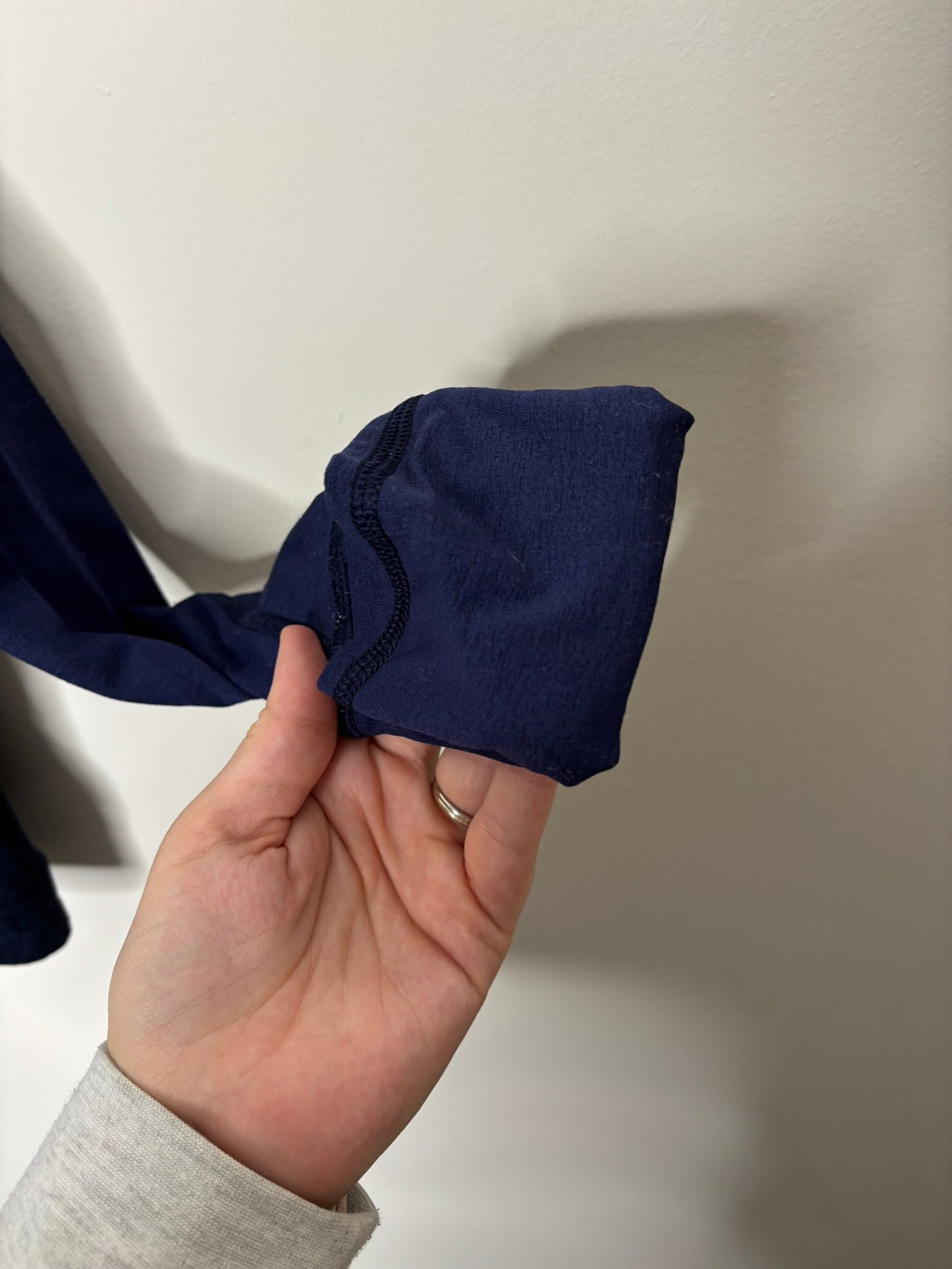 Navy blue full-zip jacket with a high neck and front pockets, hanging on a hanger against a white brick wall.