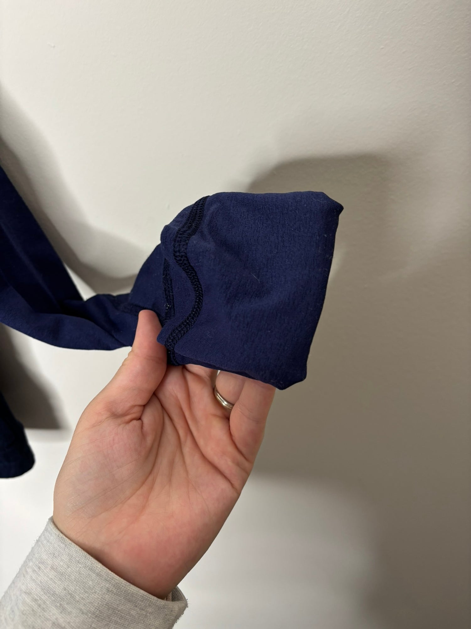 Navy blue full-zip jacket with a high neck and front pockets, hanging on a hanger against a white brick wall.