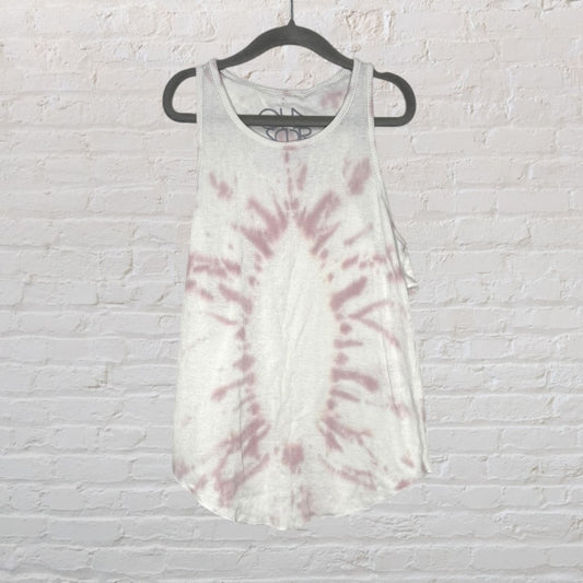 White and pink tie-dye tank top hanging on a black hanger against a brick wall.