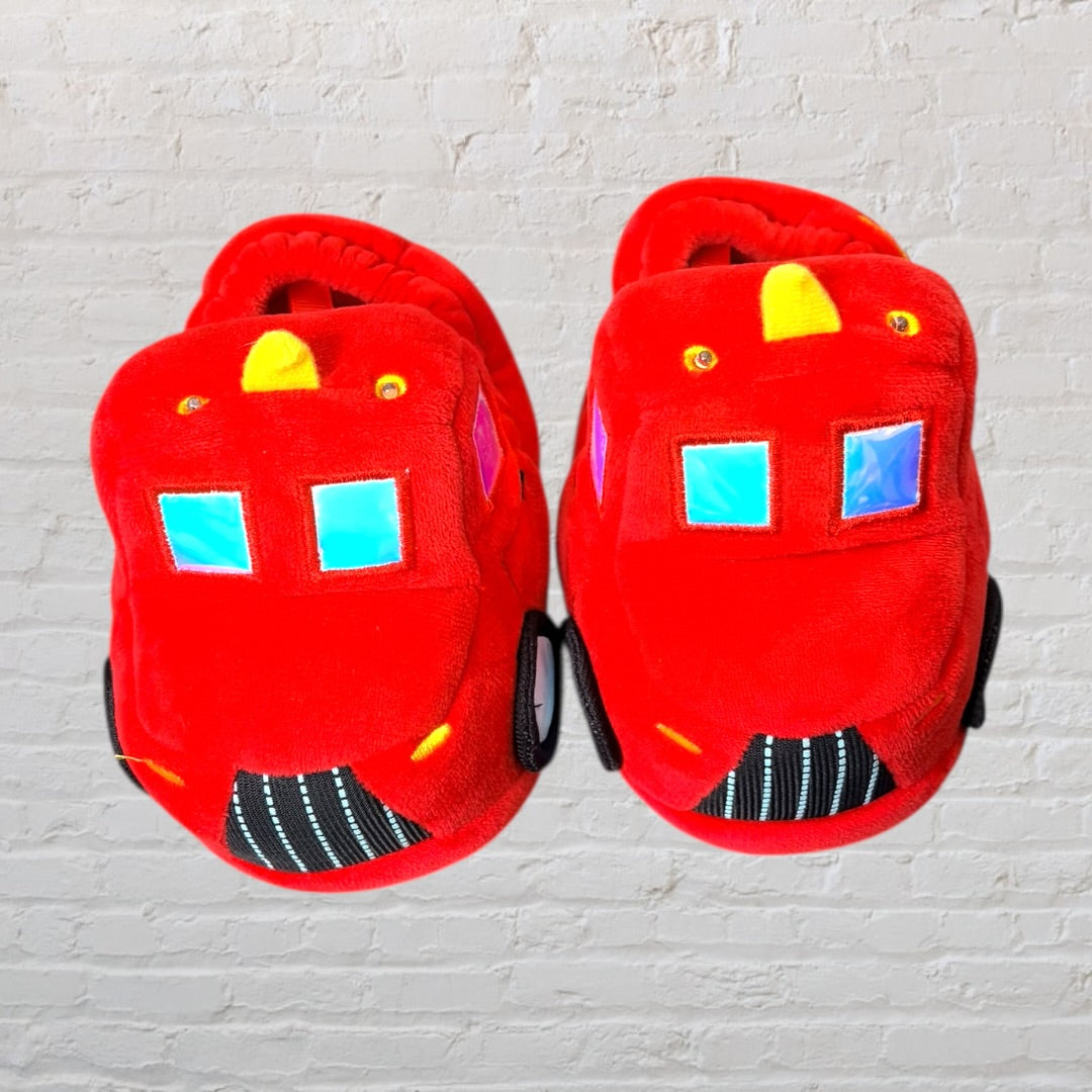 Bright red plush slippers shaped like fire trucks with black wheels and window details.
