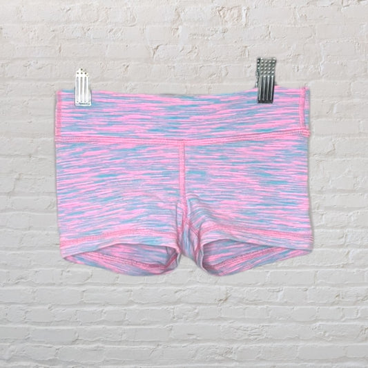 Pink and blue heathered athletic shorts hanging against a white brick background.