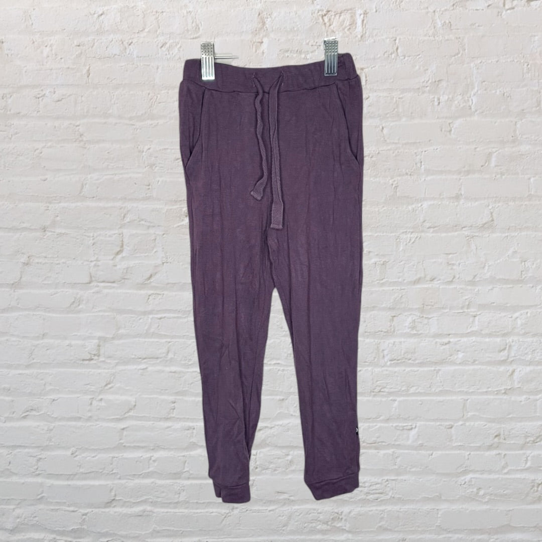 Purple long-sleeve top and pants pajama set for kids by Kyte, size 4T, displayed on a hanger against a brick wall.