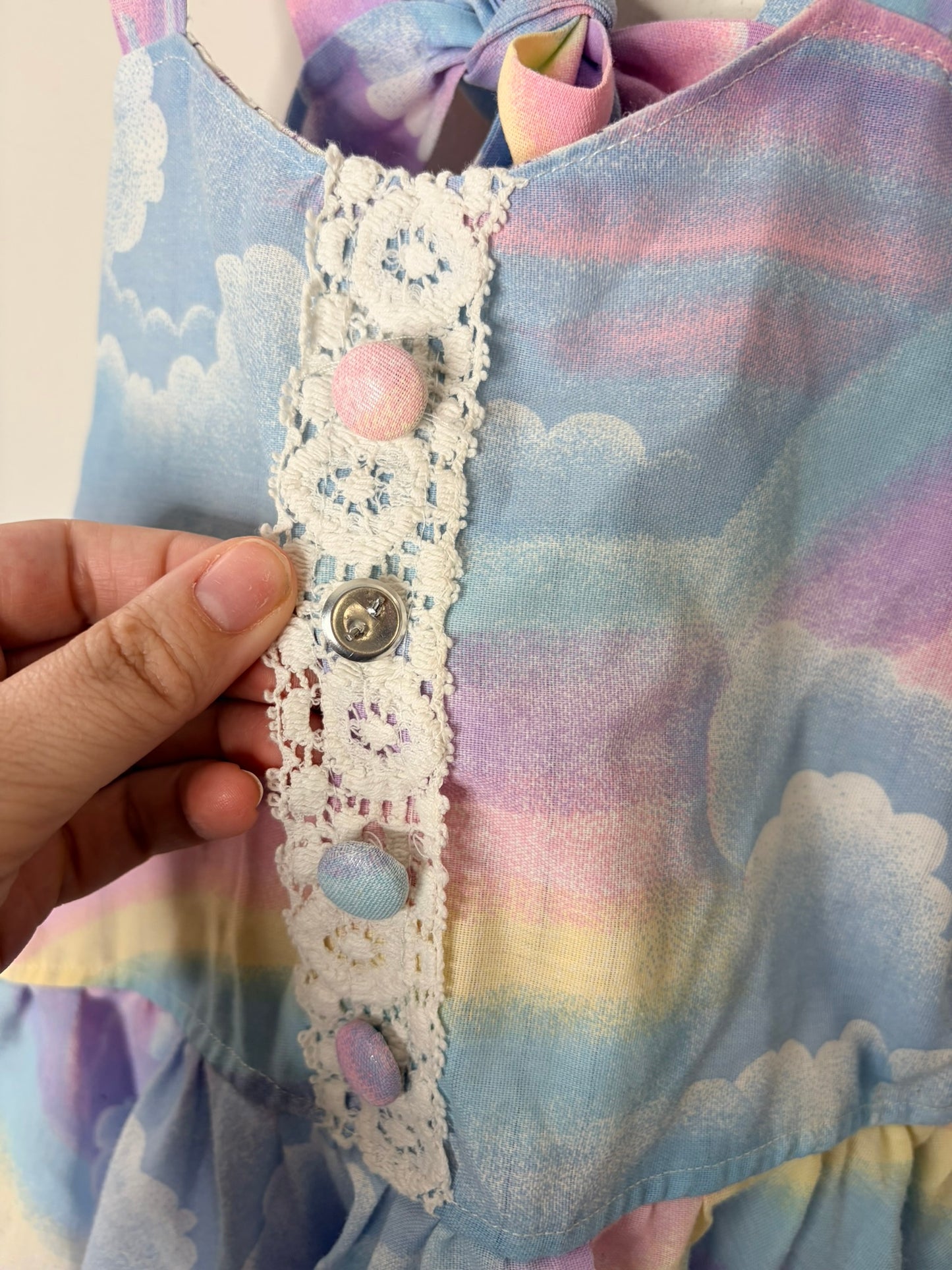 Children's dress with pastel rainbow and cloud print, featuring a ruffled hem and tied straps.