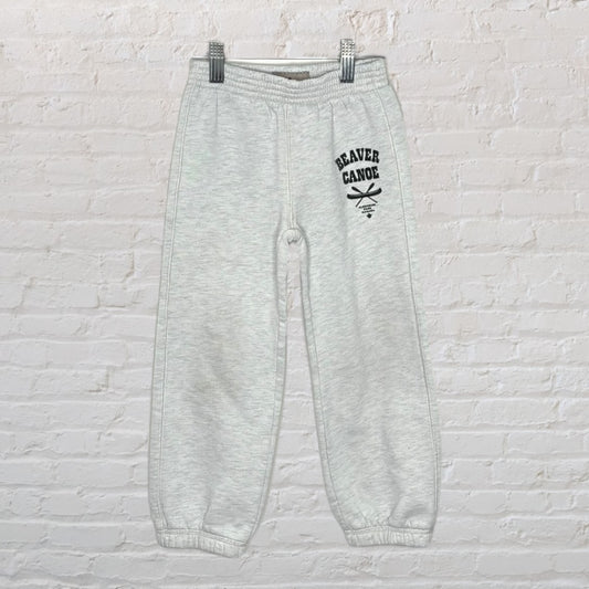 Light grey Beaver Canoe sweatpants with logo, hanging against a white brick wall.
