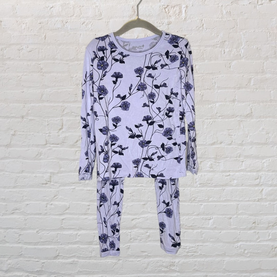 Lavender long sleeve pajama set with black floral design hanging against a white brick wall.