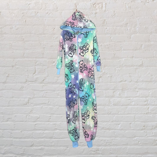 A pastel tie-dye onesie with bear prints and a hood, featuring light blue cuffs, hanging against a brick wall.