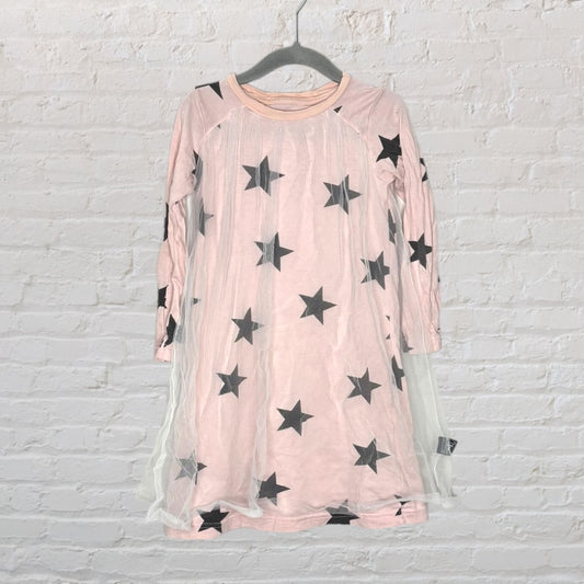 Pink long sleeve dress with black star prints and a delicate tulle overlay, hung against a white brick wall.