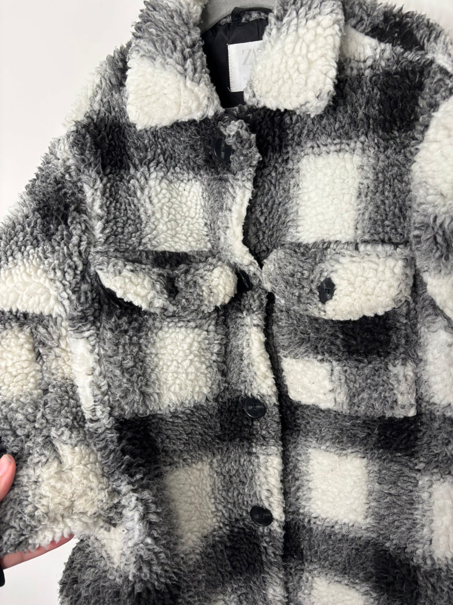 Black and white plaid Sherpa shacket with button-down front and chest pockets, hanging on a hanger.
