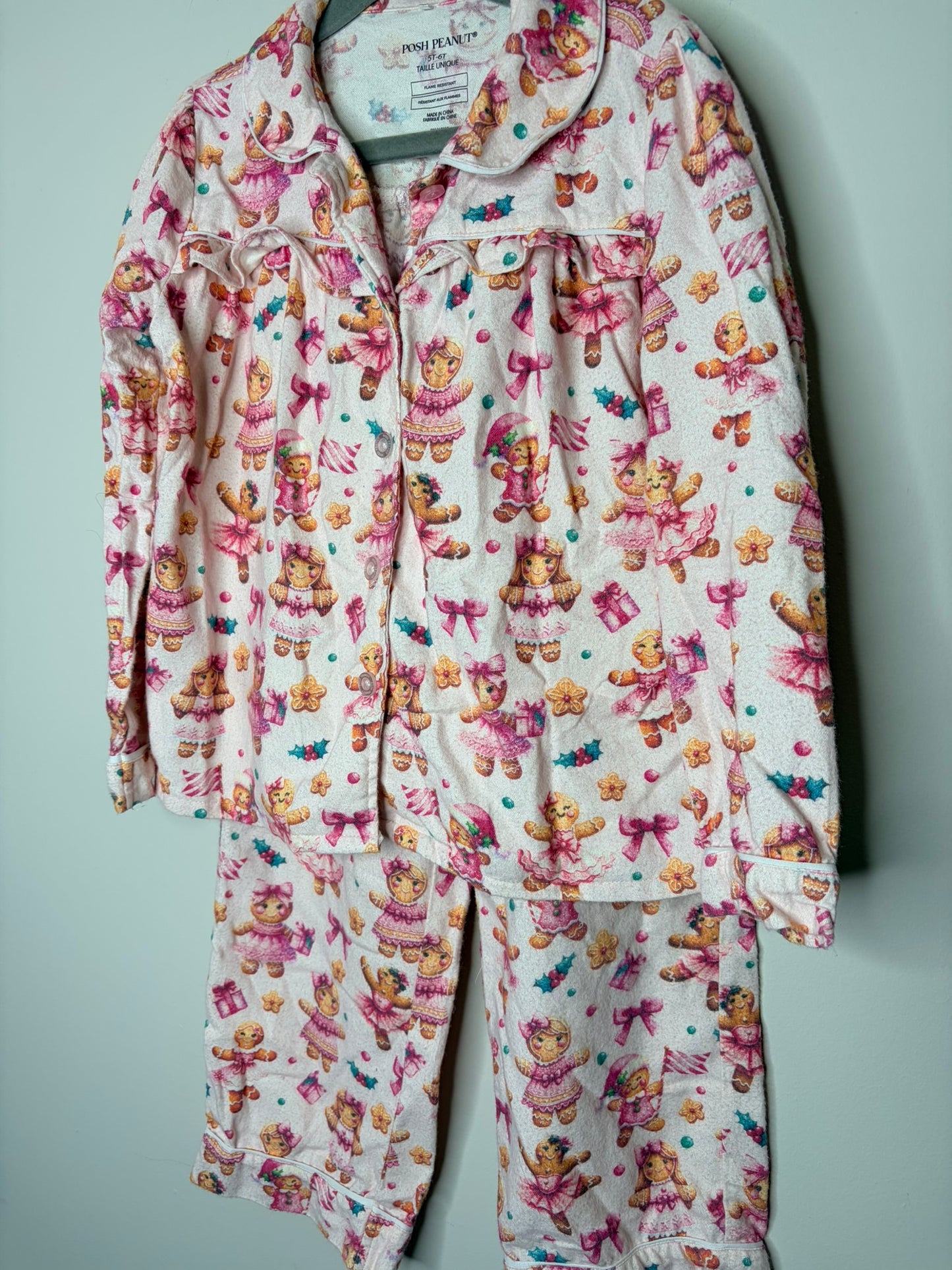 Pink pajama set with bear and bow print, featuring a button-up top and pants, hanging on a hanger.