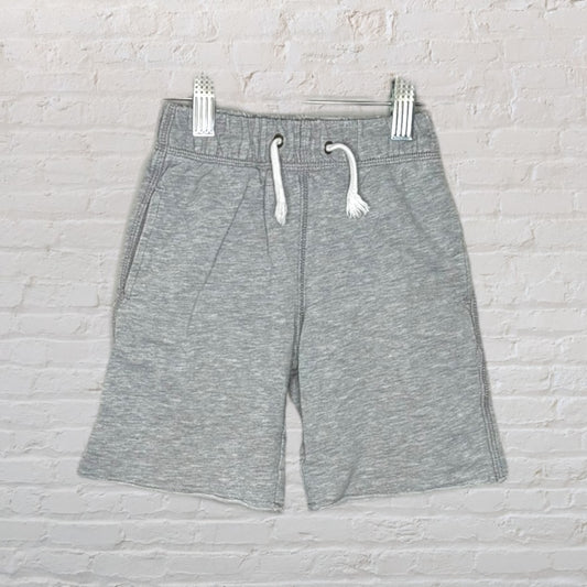 Grey sweatshorts with a drawstring waistband hanging against a white brick wall.