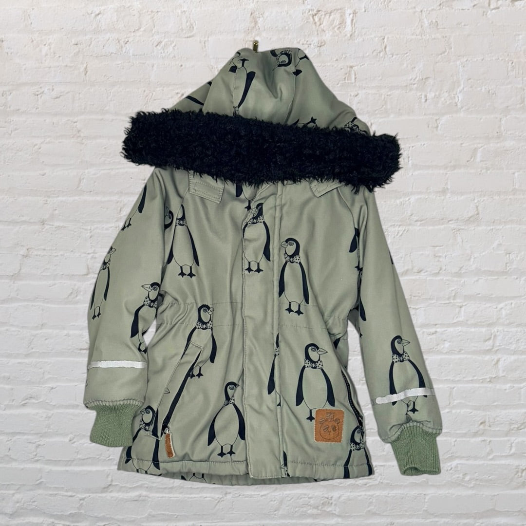 Green hooded parka with black penguin print and faux fur trim, showcased against a white brick wall.