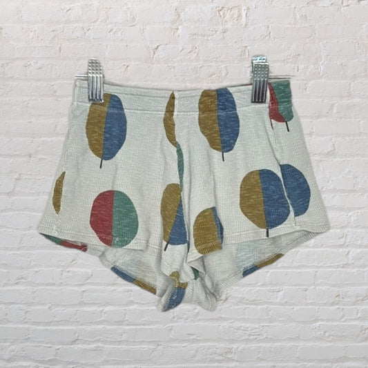 White shorts featuring a colorful geometric print with large round shapes in blue, green, red, and mustard.