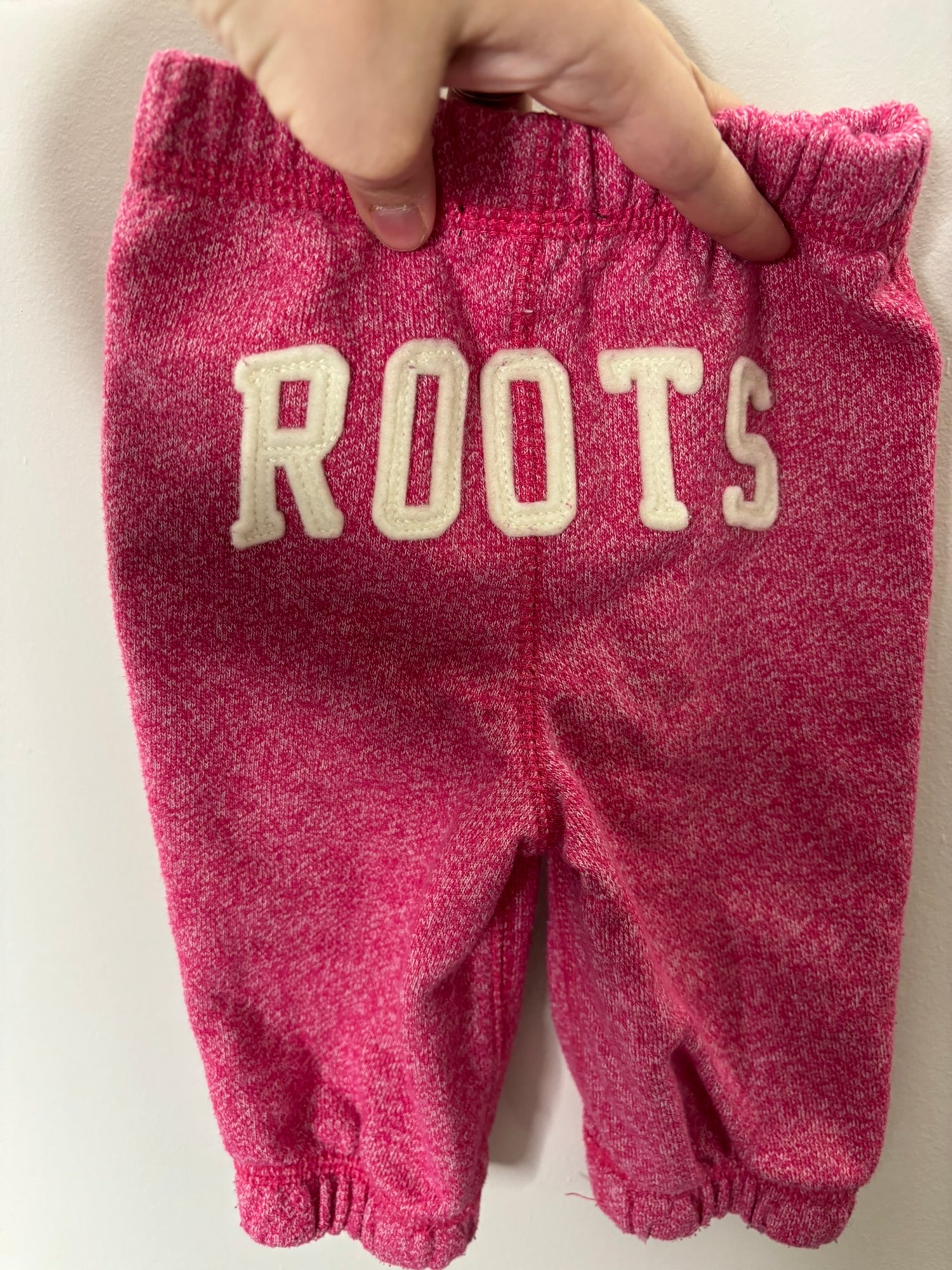 Pink toddler tracksuit set by Roots with hoodie and pants, featuring logo and maple leaf design.