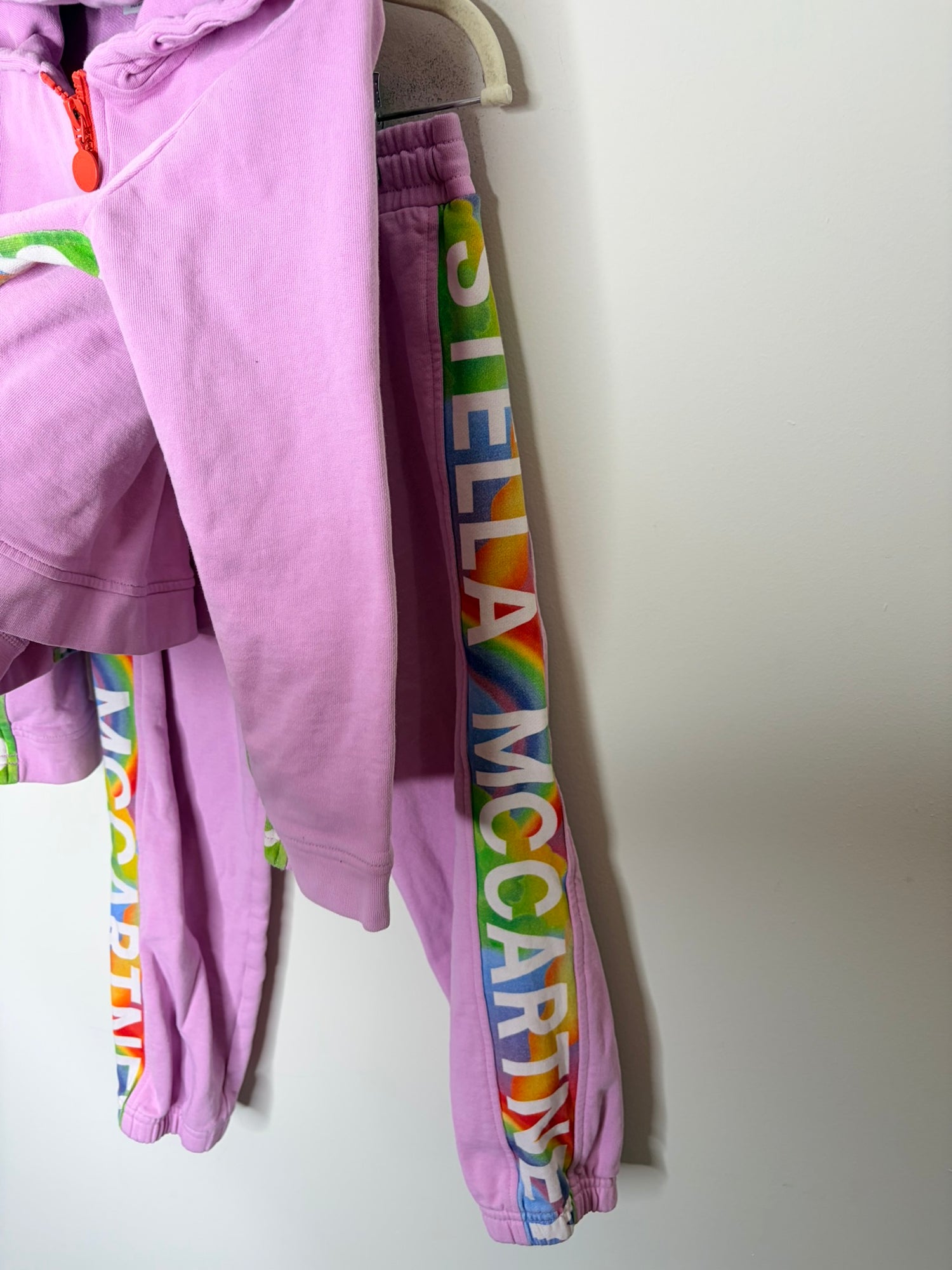 Pink tracksuit set with a hoodie and pants featuring rainbow Stella McCartney logos along the sleeves and legs.