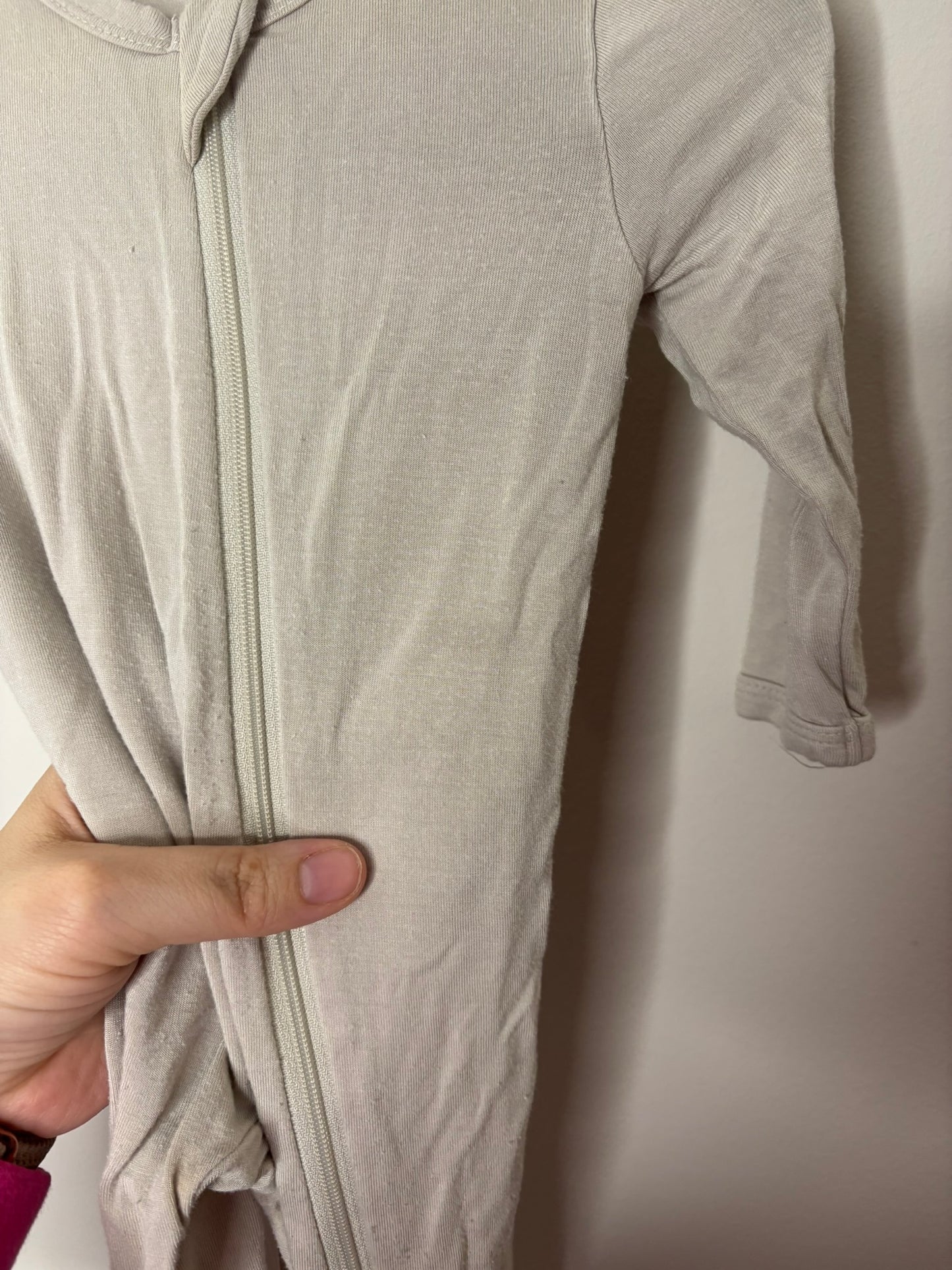 Light grey baby onesie with a zip-up front and footed design, hanging on a black hanger.