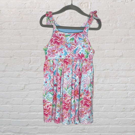 A floral sundress with ruffle straps featuring pink, blue, and green flowers, hanging on a gray hanger.