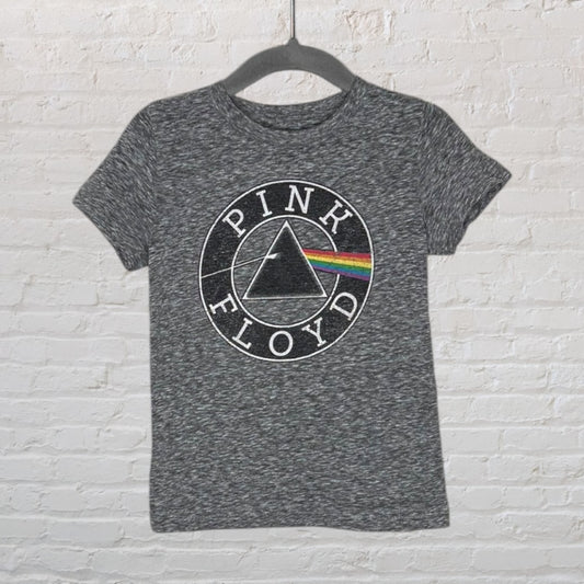 Charcoal grey T-shirt with Pink Floyd prism logo, hanging on a hanger against a brick wall.