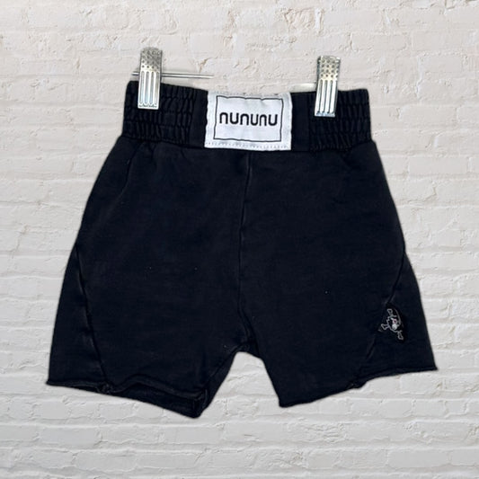 Nununu black shorts with logo displayed against a white brick background.