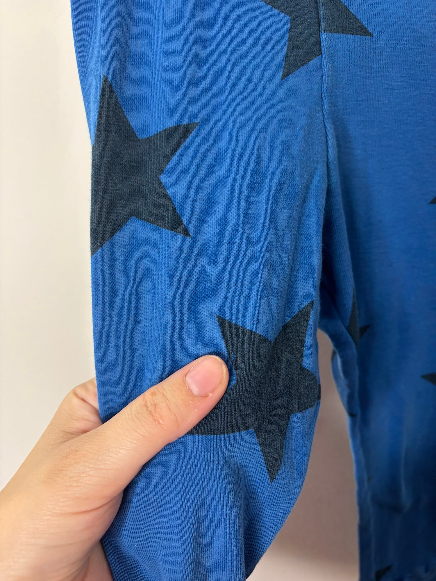 Blue leggings with black star prints and a branded waistband reading 'nununu', hung on a white brick wall background.