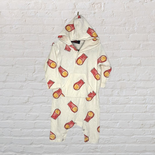 Cream hooded baby romper with red and yellow log pattern against a white brick wall.