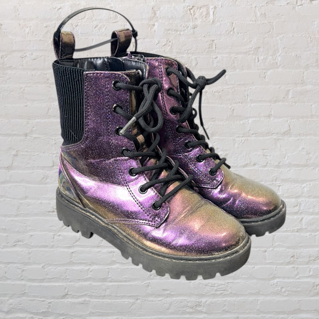 Pair of iridescent combat boots with black laces and thick soles against a white brick wall.