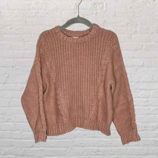 Dusty pink cable knit pullover sweater with a crew neckline, displayed on a hanger against a white brick wall.