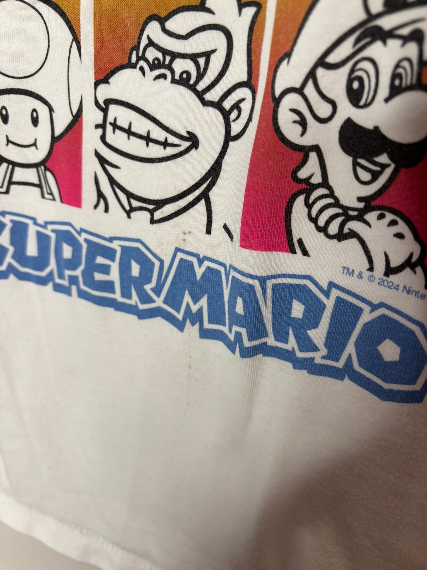 White T-shirt featuring Super Mario character graphics in a grid layout, hanging on a black hanger.