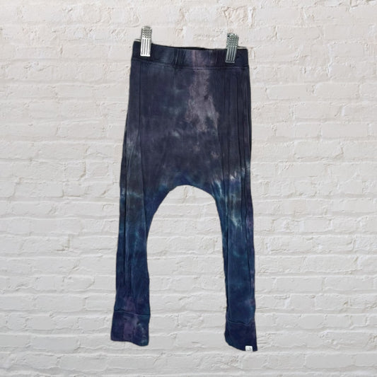 Dark blue and purple tie-dye drop crotch leggings hanging against a white brick wall.