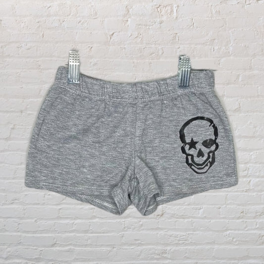 Gray shorts with a black skull graphic design, displayed on a white brick background.