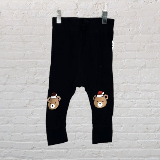 Black leggings with festive bear prints wearing Santa hats, hung against a white brick wall.