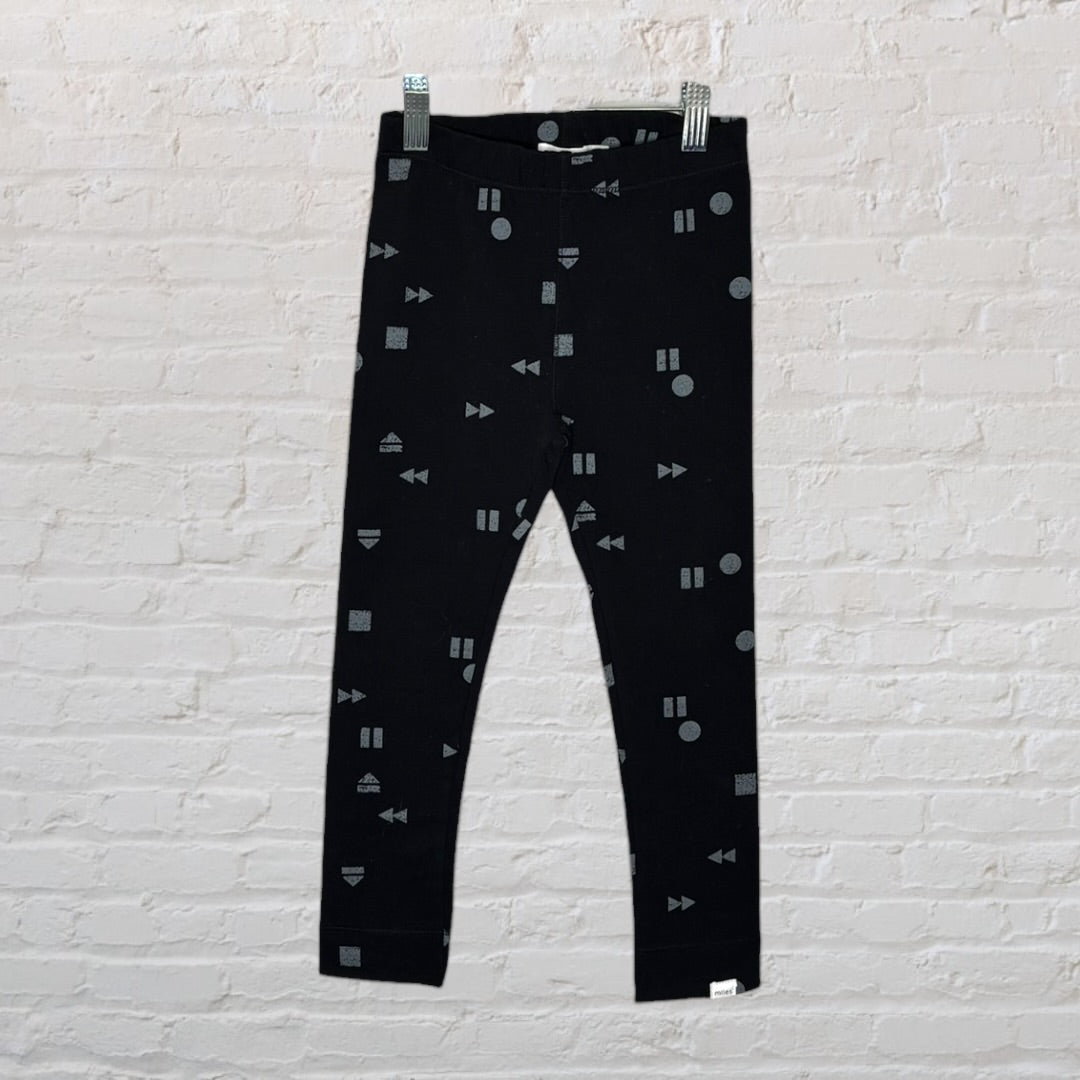 Black leggings with geometric grey patterns hanging against a brick wall background.