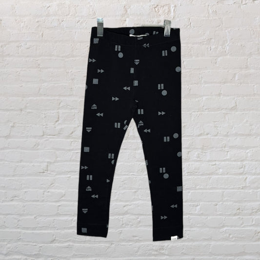 Black leggings with geometric grey patterns hanging against a brick wall background.