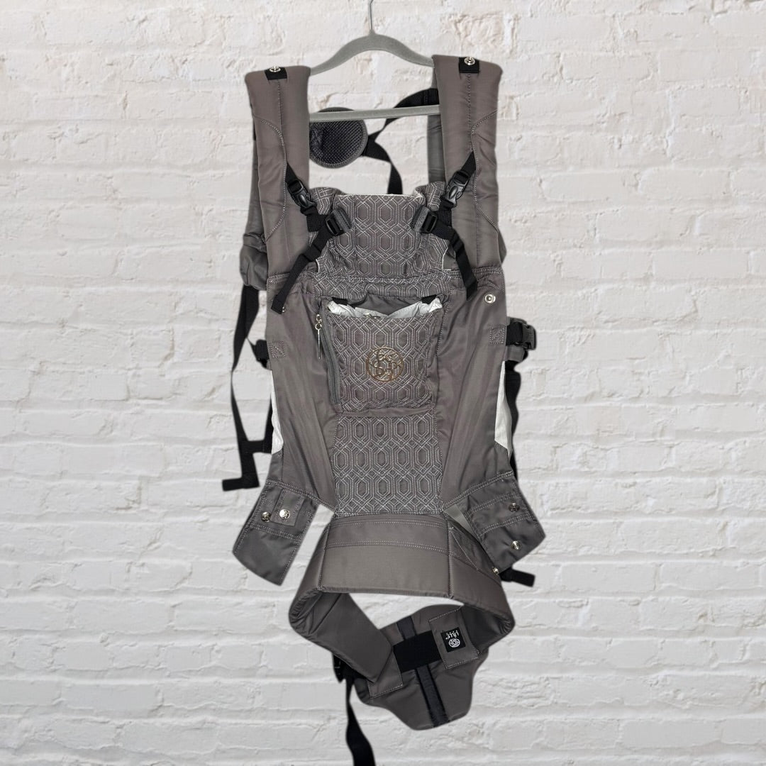 Gray ergonomic baby carrier with multiple straps and support, hanging on a hanger.