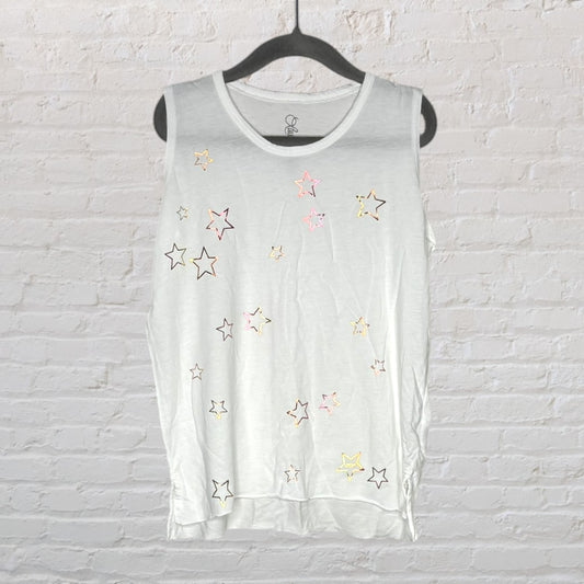 White sleeveless top with multicolored star pattern, hanging on a black hanger against a brick wall.