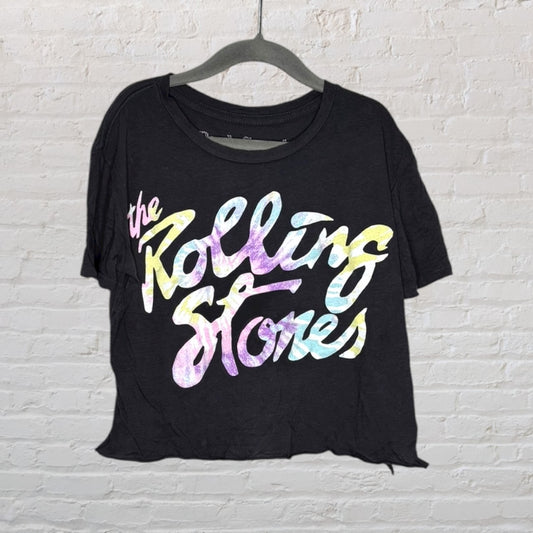 Black T-shirt featuring a colorful pastel gradient 'Rolling Stones' text graphic, hung on a hanger against a white brick wall.