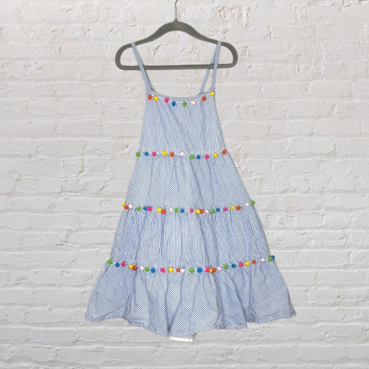 Blue and white striped sundress with tiered skirt and colorful pom pom trim hanging on a black hanger.
