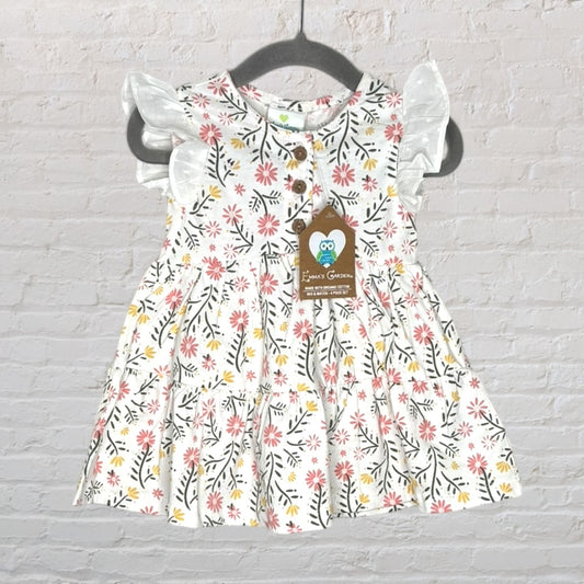 White dress with pink and yellow floral pattern, ruffle sleeves, and wooden buttons, tagged with 'Emma's Garden', hanging on a dark hanger.
