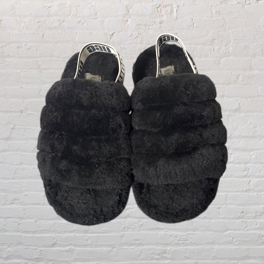 Black fluffy slingback slippers by UGG with elastic UGG-branded strap.