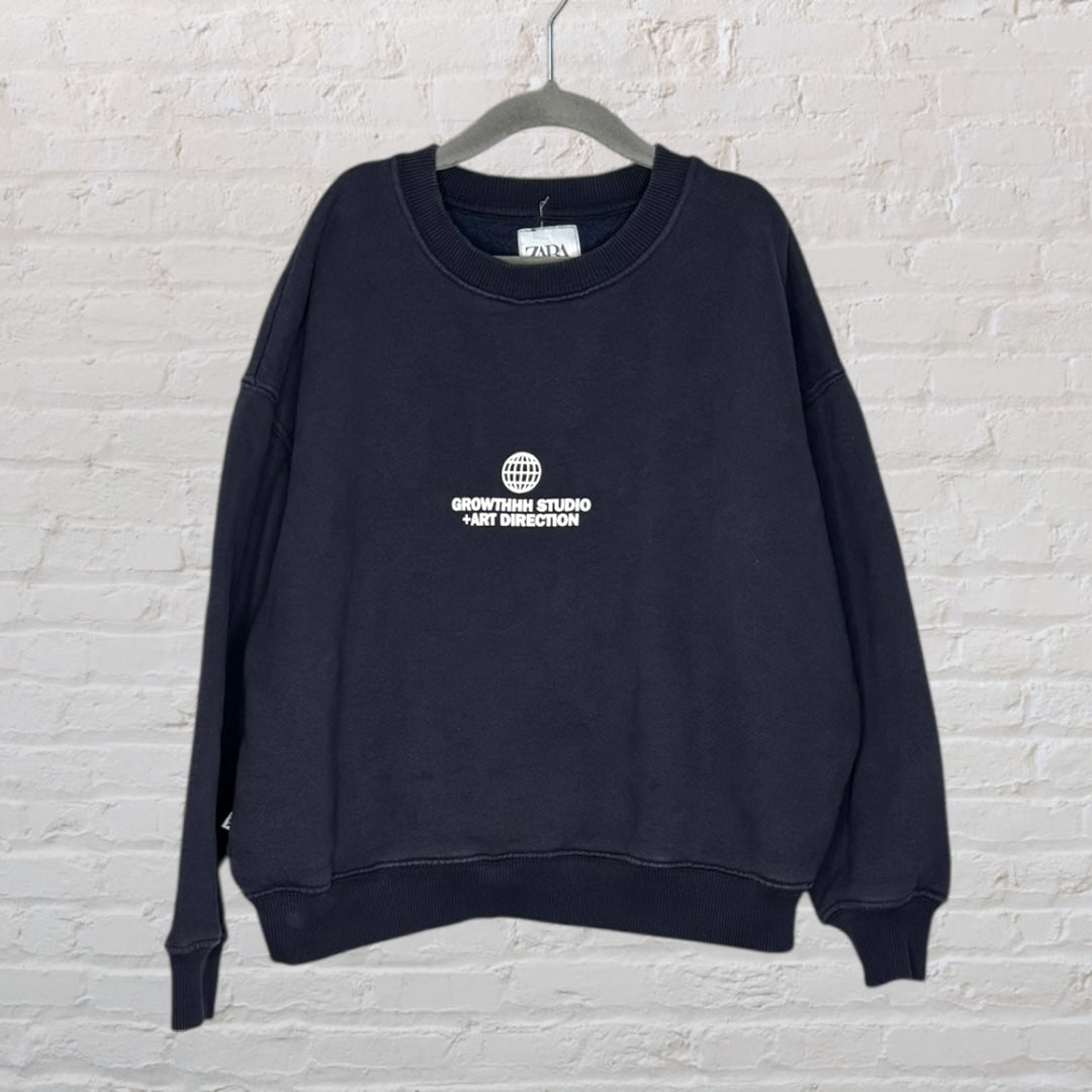 Black sweatshirt with 'Updated Tribe' graphic print on the back, hanging against a brick wall.